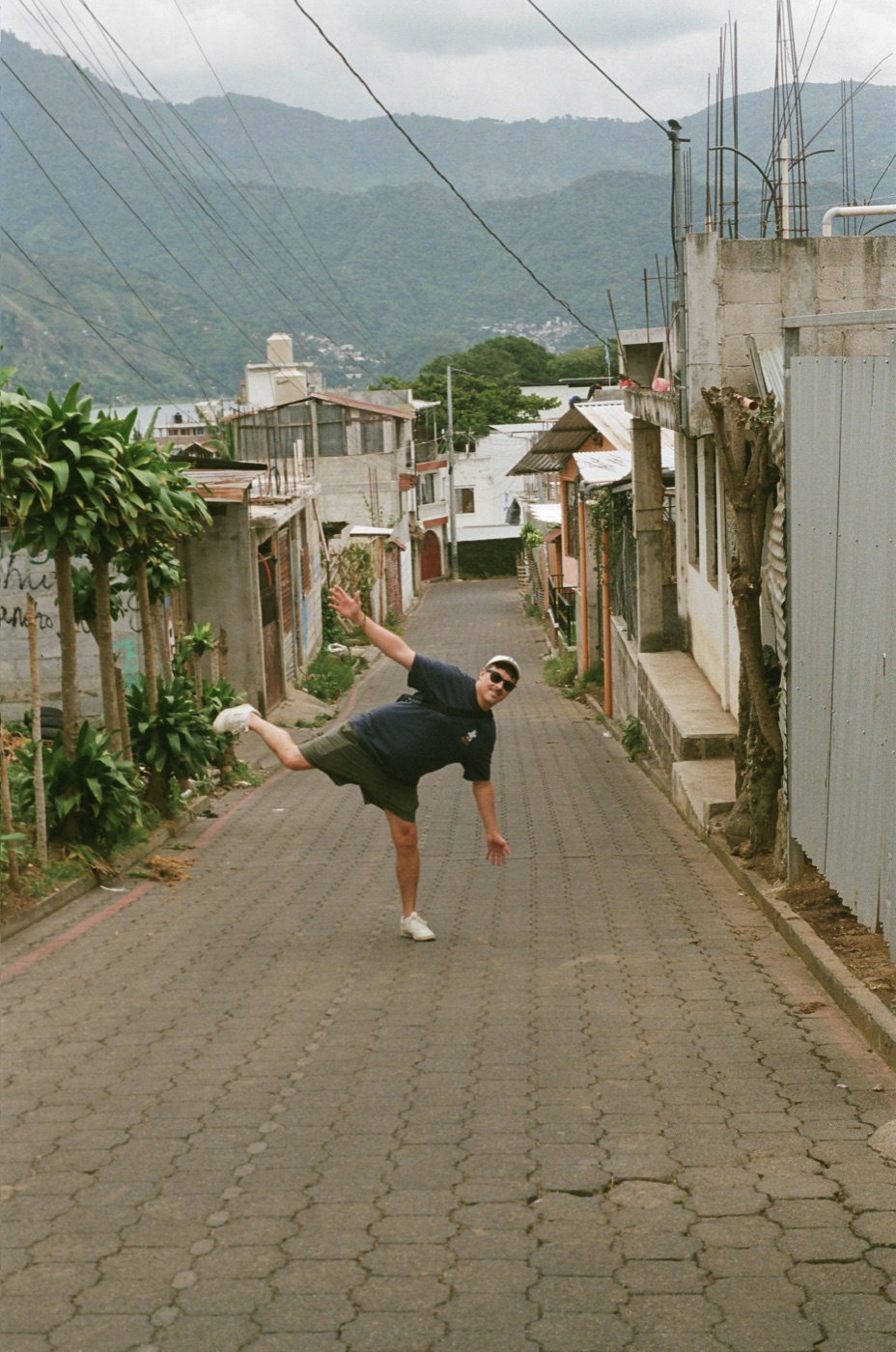 Luke Little mid-kick on a steep cobblestone street, with mountains behind him